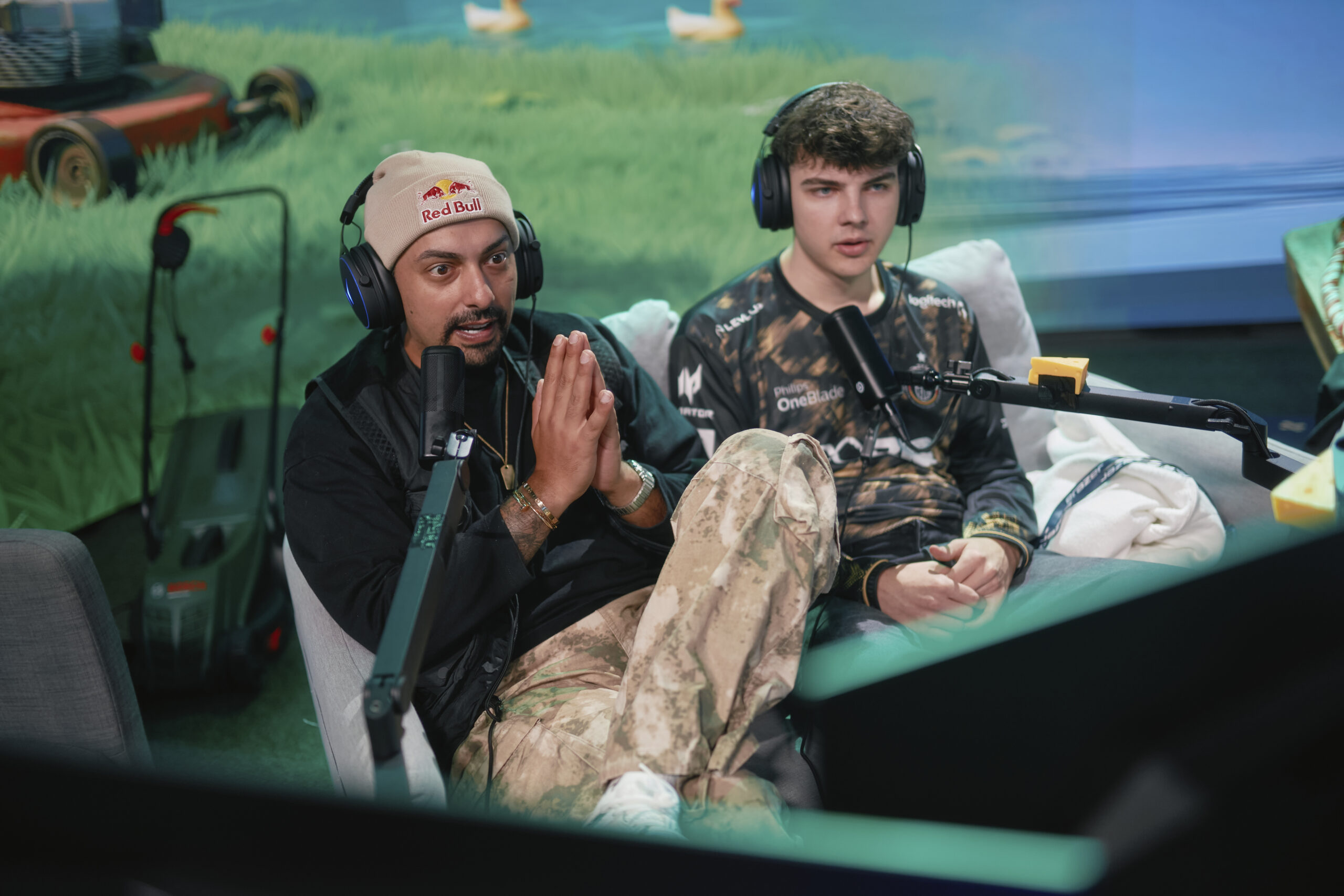 Creator Amar sitzt links mit Headset und Mikrofon auf einem Sofa und moderiert das ERAZER YR2V Esports-Turnier für die DACH-Region. Neben ihm sitzt sein Co-Host mit Headset vor einem zweiten Mikrofon.