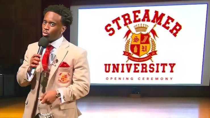 Bild 1: Kai Cenat im beigen Anzug mit Mikrofon bei der Eröffnungszeremonie der Streamer University. Hinter ihm zeigt ein Bildschirm das rote Veranstaltungslogo.